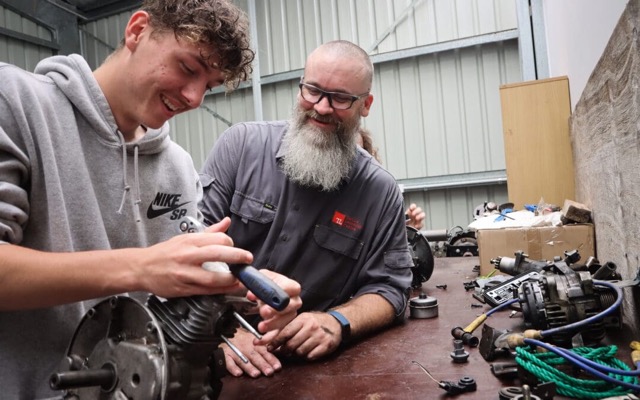 Automotive Students working in front of single cylinder on a car workshop with his trainer