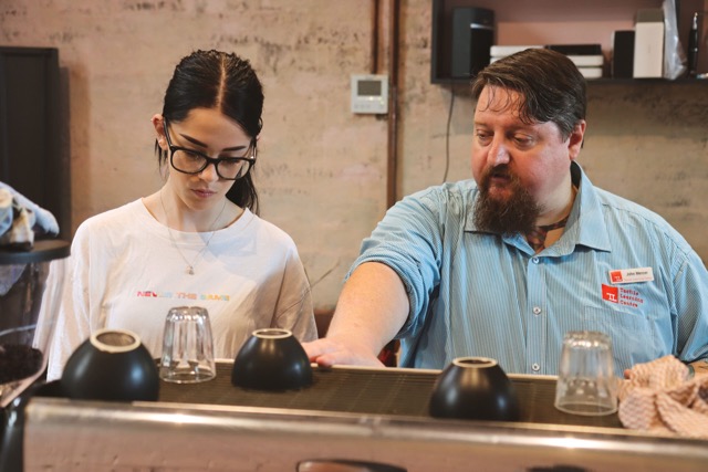 Hospitality trainer working with a student in front of coffee machine